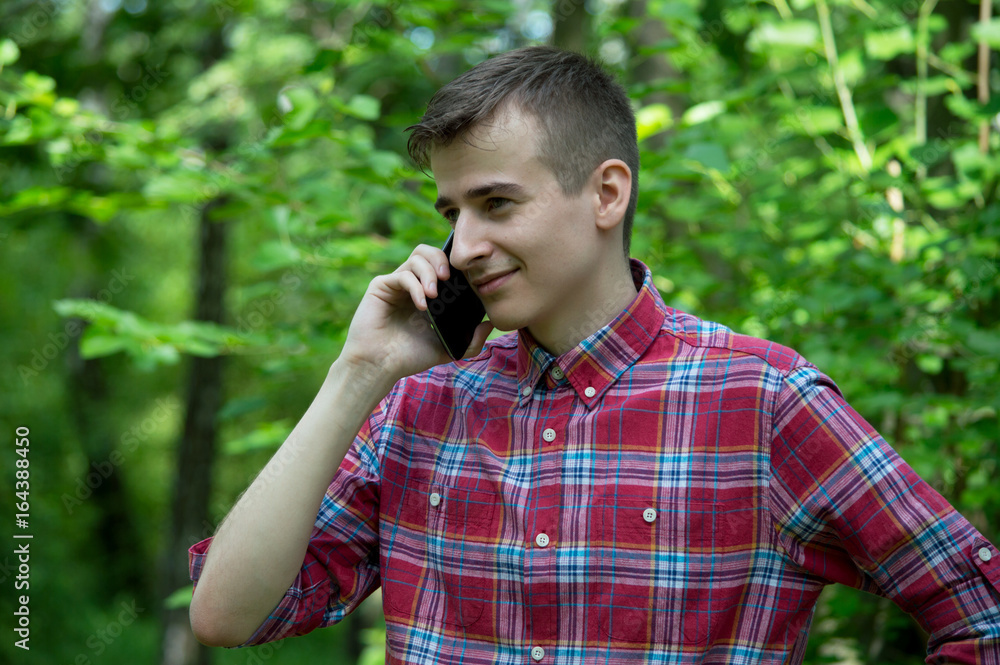 A guy smiles and talks on the phone in the park. A guy smiles and talks on the phone in the park.