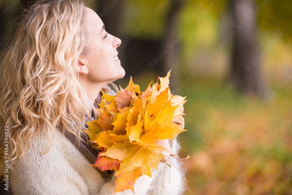 Naklejka premium Portrait of young woman with maple leaves on autumn sunset background. Girl walking in the park and enjoying sunny weather. Lifestyle and autumn concept