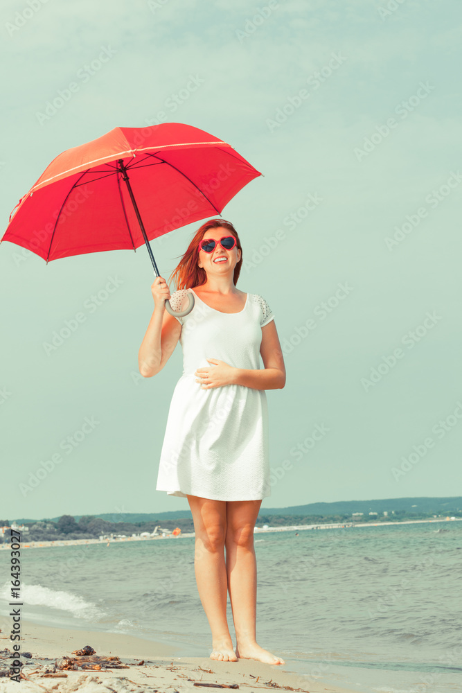 Redhead woman walking on beach holding umbrella