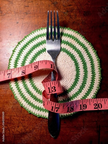 Pink tape measure coiled around a fork on a wood table. Illustration for weight loss goals, food and nutrition, healthy lifestyle, eating disorders. photo