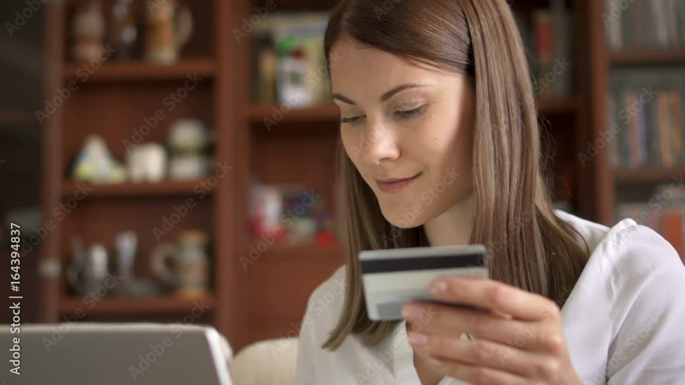 Businesswoman in white blouse sitting on sofa in living room buying online with credit card on laptop Businesswoman in white blouse sitting on sofa in living room buying online with credit card on laptop