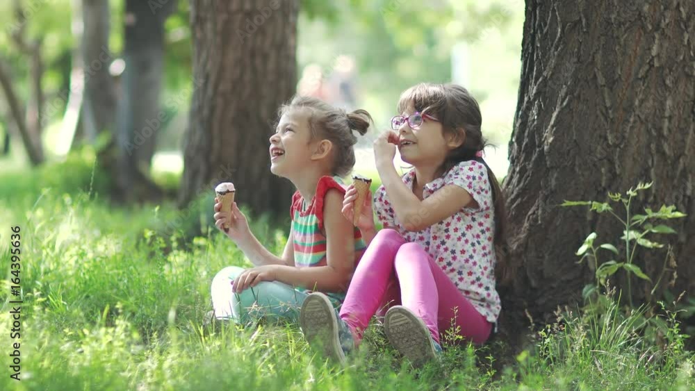 sisters sit on the grass in the summer Park and eat ice cream. happy carefree childhood