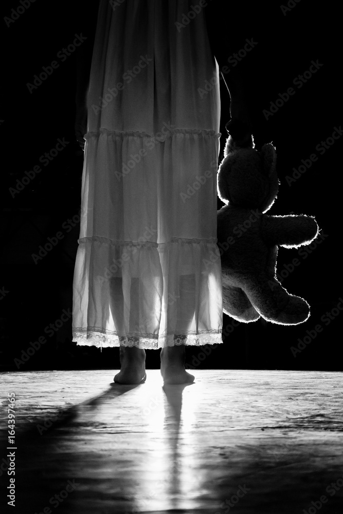a girl holding a teddy bear in the darkness
