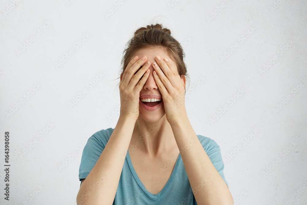 Happy woman closing her eyes with hands going to see surprise prepared by her husband standing and smiling in anticipation for something wonderful. Young cheerful lady covering her face with hands