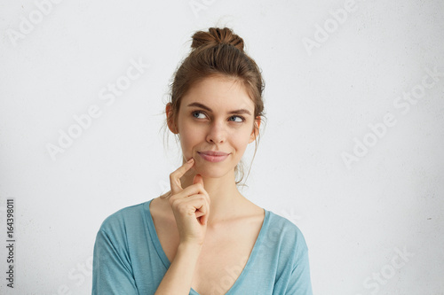 Dreamy young woman looking thoughtfully aside holding her finger on chin dreaming about honey moon with her future husband. Thoughtful female with attractive female having ideas or planning something photo