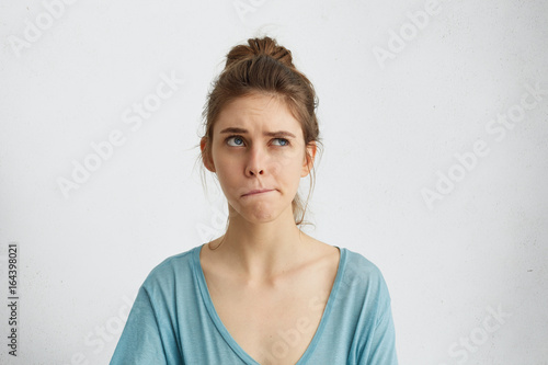 Portrait of doubtful and pensive woman looking up and curving her lips trying to make decision. Irresolute female thinkig something over while posing in studio. People, youth, beauty, body language photo