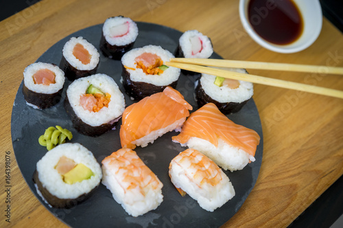 Sushi with wasabi on a wooden table on black slate plate with soy sauce and chopsticks
