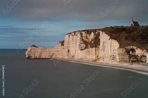 The church on top of the cliffs at Etretat in Normandy, showing the pebble beach and the natural arch called Porte d’Amont