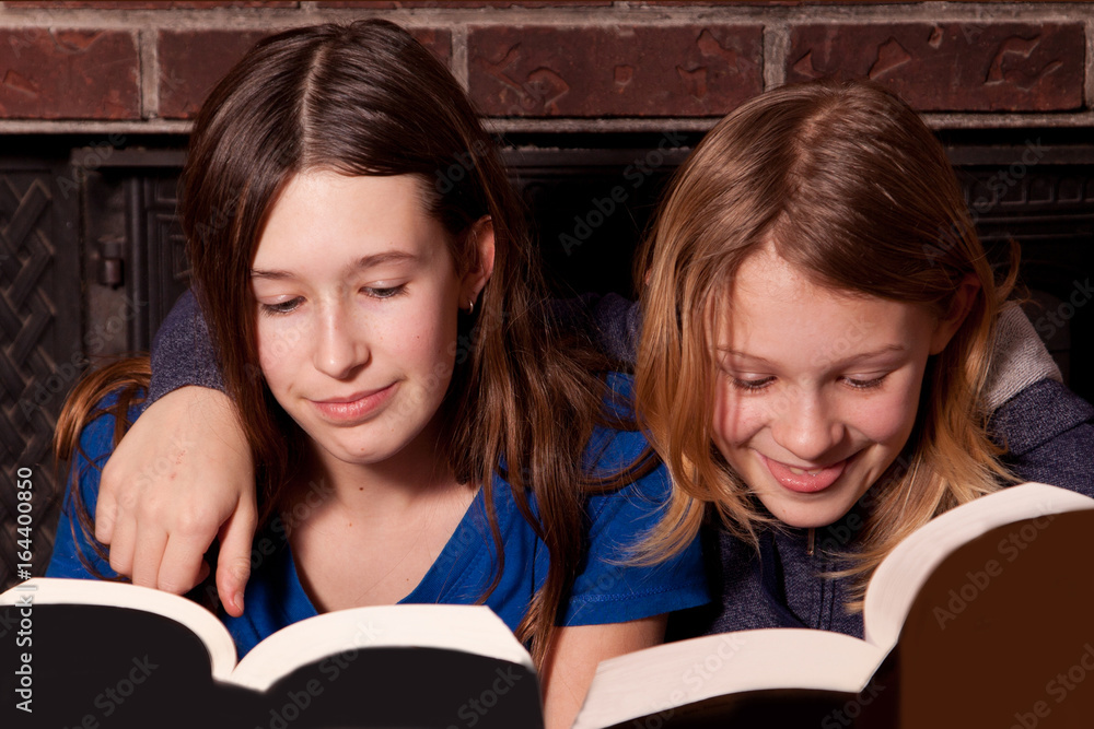 Two sisters reading books together with arms around their shoulders. Two sisters reading books together with arms around their shoulders.