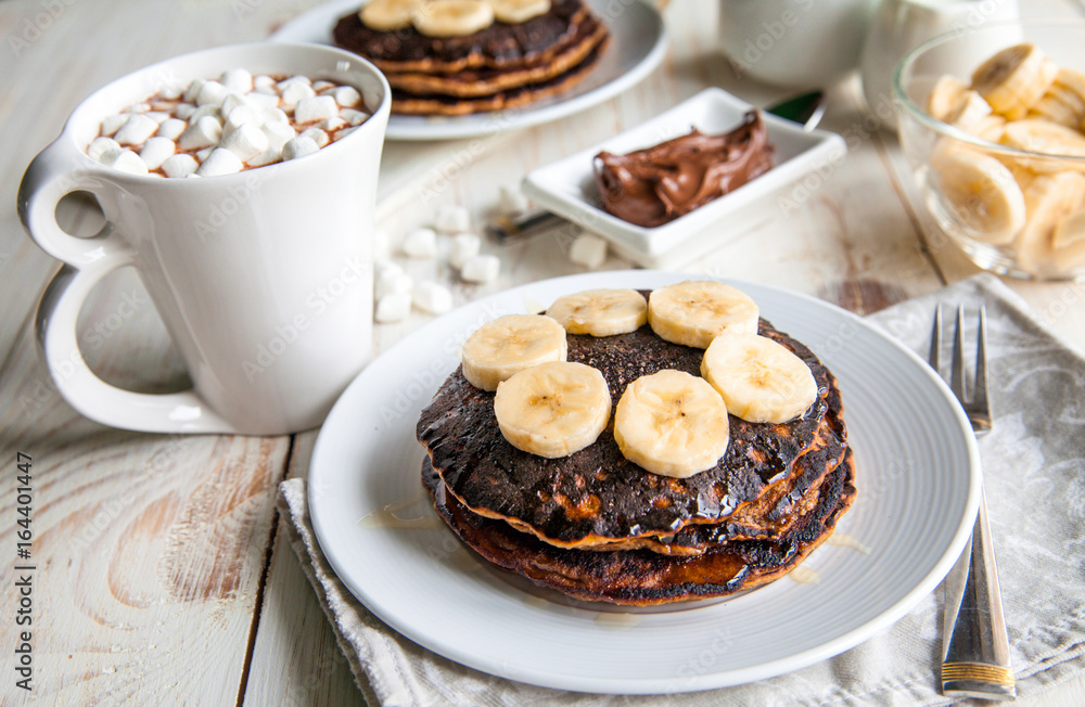 Breakfast for couple included oat pancakes with banana, nutella, honey, with coffe and milk and cacao with marshmallow on white wooden  background