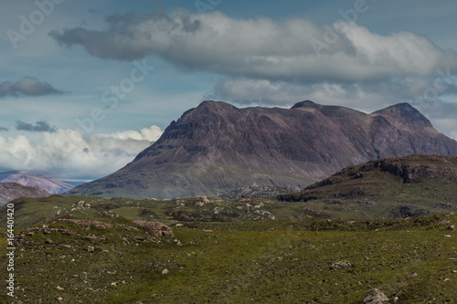 Assynt Peninsula, Scotland - June 7, 2012: Brown mountain ridge under blue skies with white and gray clouds fronted by green wild rough slopes east of Loch Buine Moire. photo