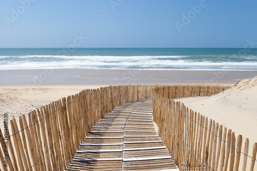 Holzweg mit Zaun verläuft in Kurve durch Dünen zum Strand, Atlantikküste