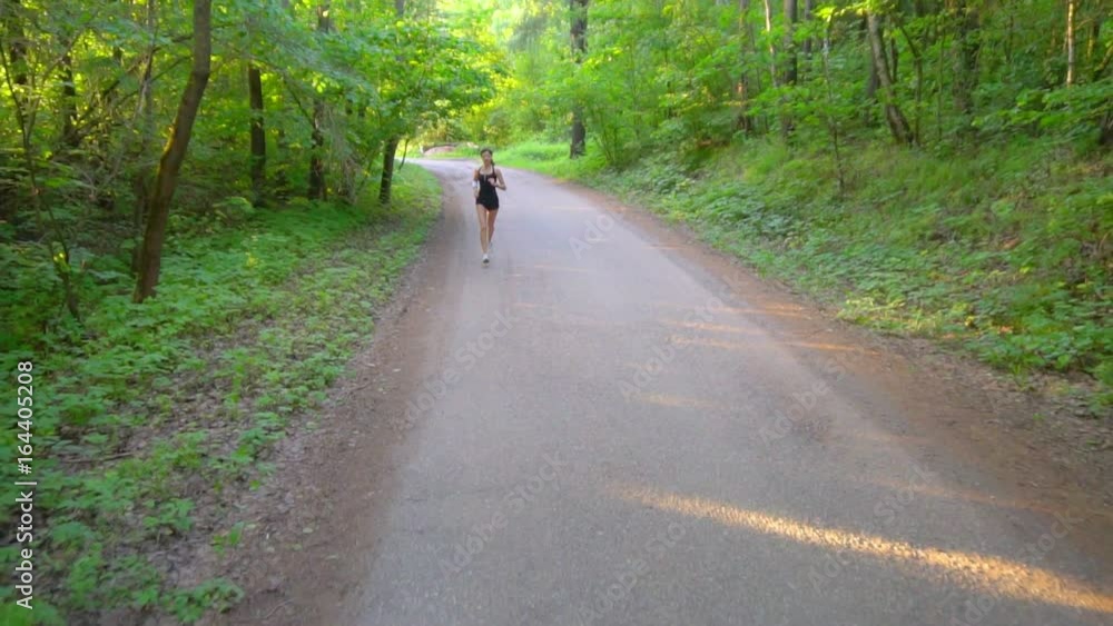 Young woman runner is running down the road in a sporty uniform