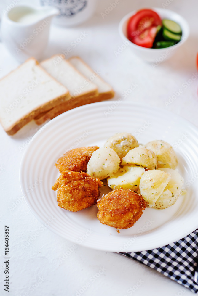 Delicious and hearty dinner, chicken balls in breading, with potatoes on a garnish with fresh tomato and cucumber, white toast, olive oil, black coffee and milk on a white background