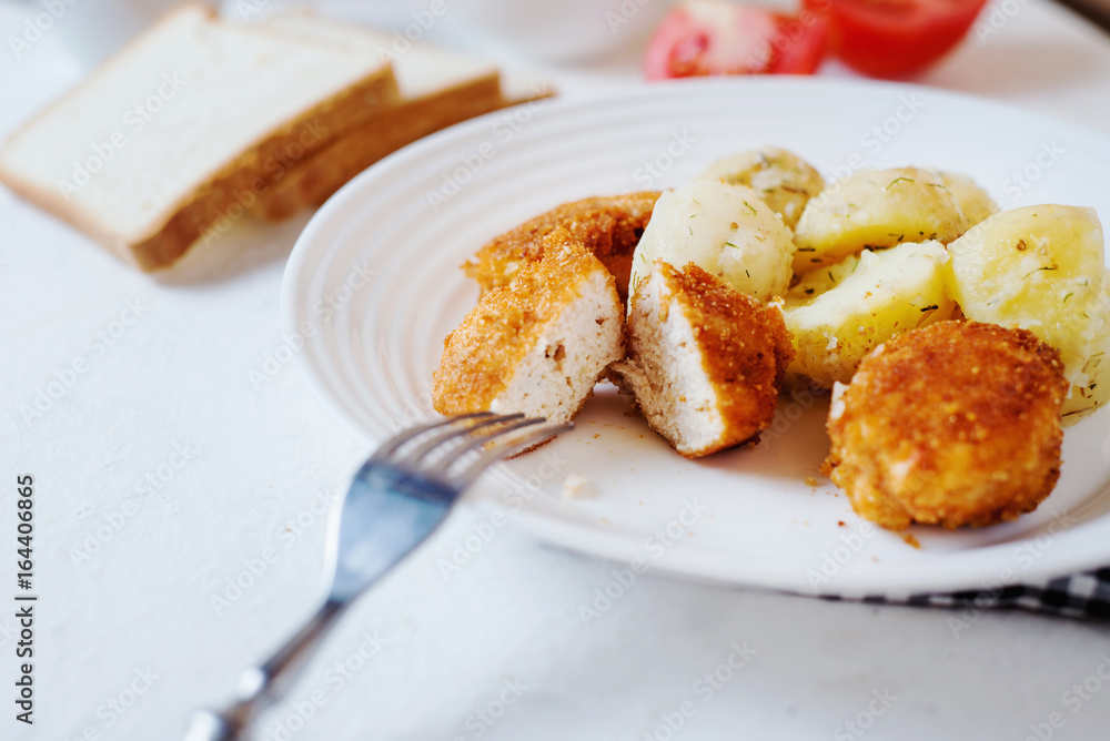 Delicious and hearty dinner, chicken balls in breading, with potatoes on a garnish with fresh tomato and cucumber, white toast, olive oil, black coffee and milk on a white background Delicious and hearty dinner, chicken balls in breading, with potatoes on a garnish with fresh tomato and cucumber, white toast, olive oil, black coffee and milk on a white background