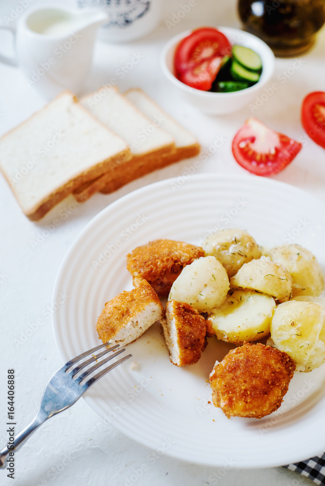 Delicious and hearty dinner, chicken balls in breading, with potatoes on a garnish with fresh tomato and cucumber, white toast, olive oil, black coffee and milk on a white background