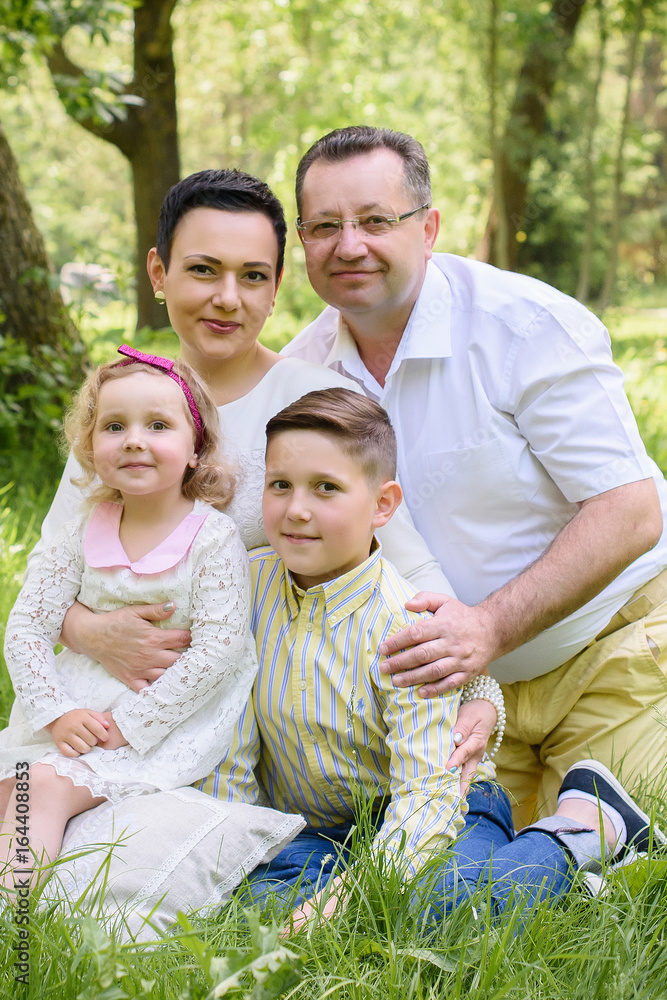 Grandfather with daughter, grandson and granddaughter relax in the park in the summer