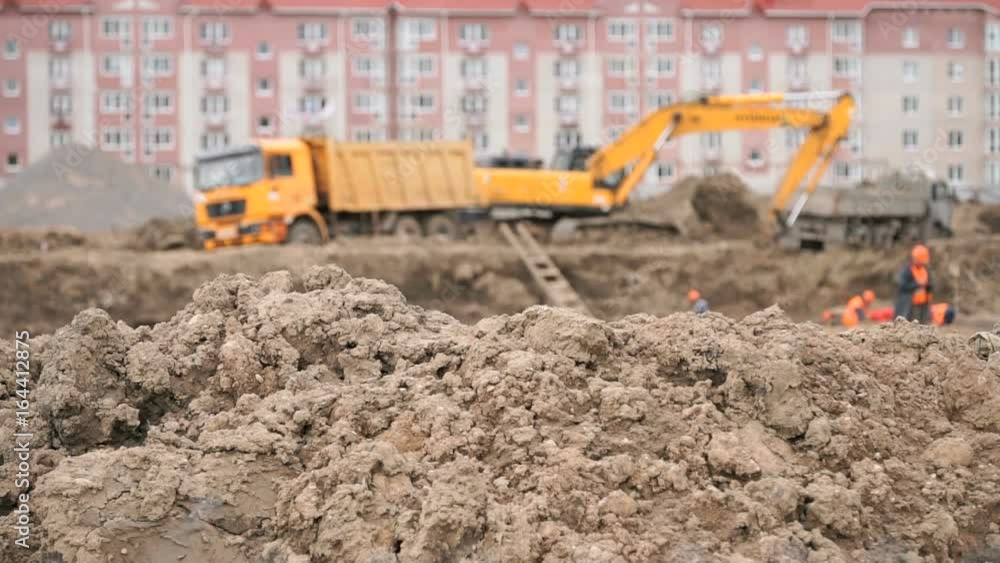 Yellow excavator loads clay using its big bucket into the dump truck on the background residential development. Construction area in summer Yellow excavator loads clay using its big bucket into the dump truck on the background residential development. Construction area in summer