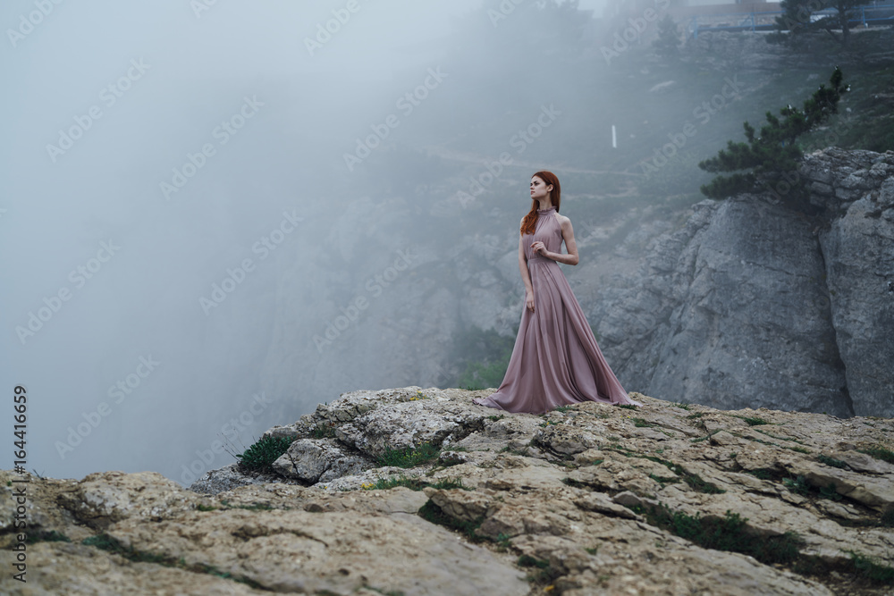 Beautiful young woman in a long pink dress is standing on a hillside Beautiful young woman in a long pink dress is standing on a hillside
