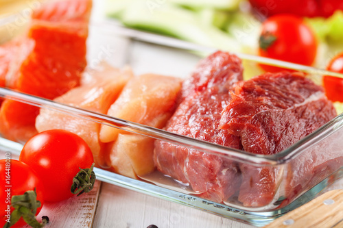 Products for a diet - raw meat of beef and chicken, a salmon and vegetables on a light wooden background. Selective focus.