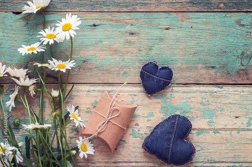 Bouquet of daisies with gift box and denim hearts on old wooden background. Place for text.