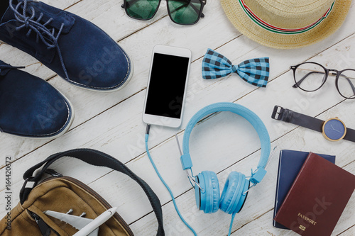 Top view accessoires to travel concept.mobile phone listening music by headphone on wooden background.Man'shoes,airplane,bag,passport,bow tie,watch,sunglasses on white wood table.flat lay.copy space.