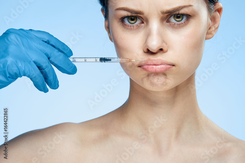 Beautiful young woman on a blue background holds a syringe, plastic, medicine