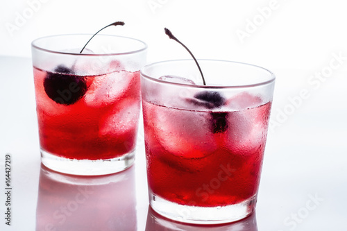 Red drink with a cherry in a glass with ice on a white background.