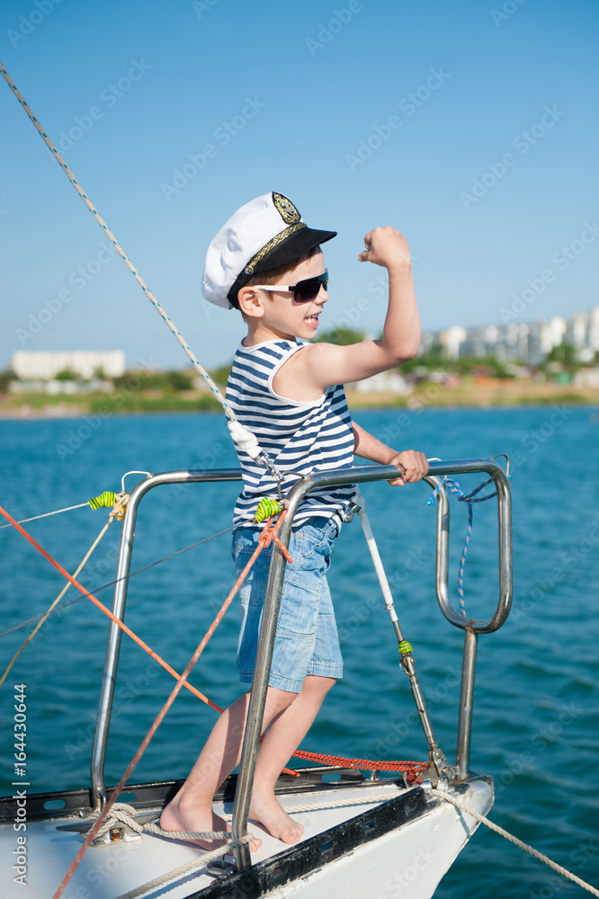 Strong and healthy kid captain showing muscles standing on board yacht