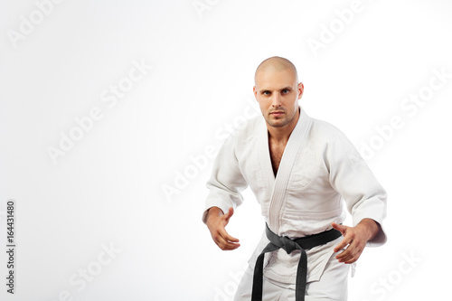 Young man fighter in white kimono with black belt for judo, jujitsu posing in combat pose on isolated white background