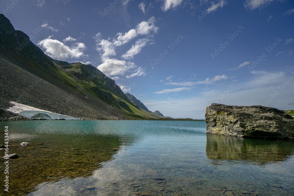 still mountain lake with reflections and a large boulder in the foreground in the Swiss Alps near Davos
