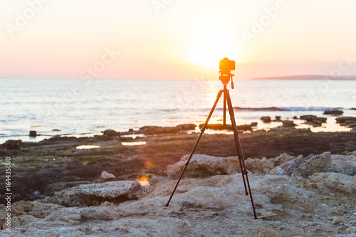 Camera with tripod over sun rising near the beach