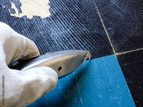 white gloved hand with carpet knife pulling up old linoleum flooring with toxic tar glue underneath photo