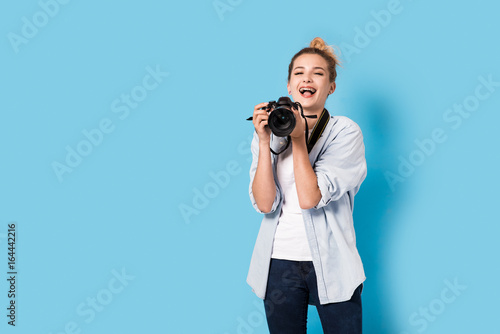 Young blonde photographer is enjoying her work. Model isolated on a blue background with copy space photo