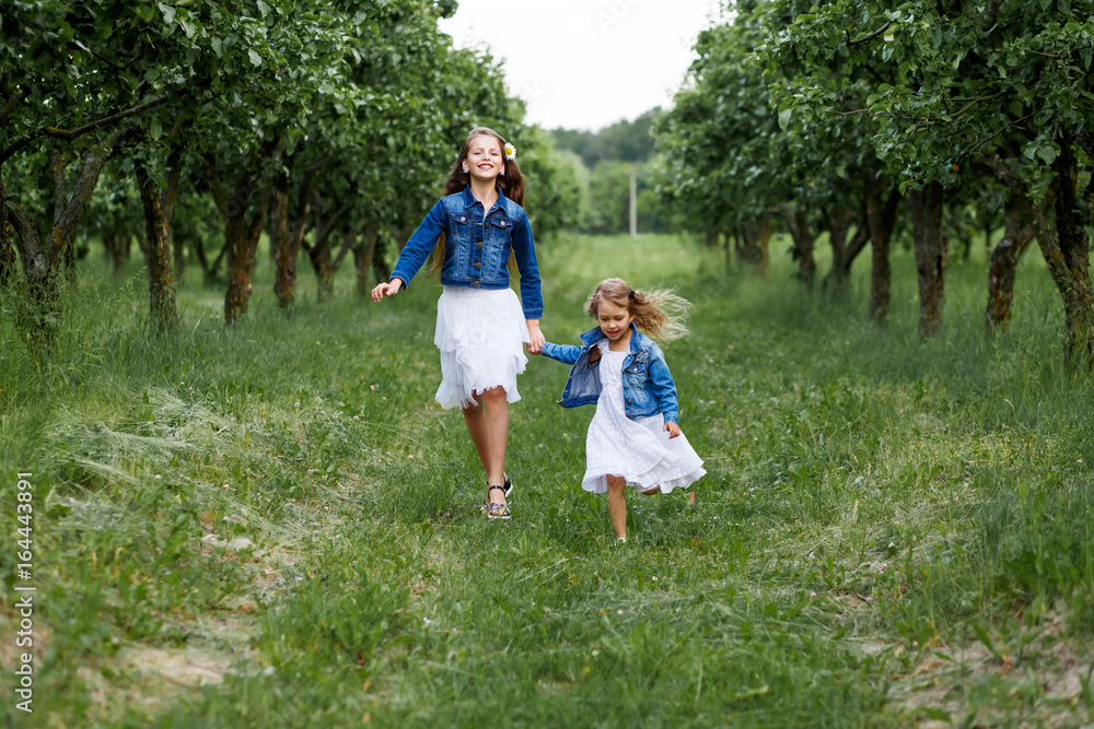 Two sisters having fun outside in summer running in the apple tree garden Two sisters having fun outside in summer running in the apple tree garden