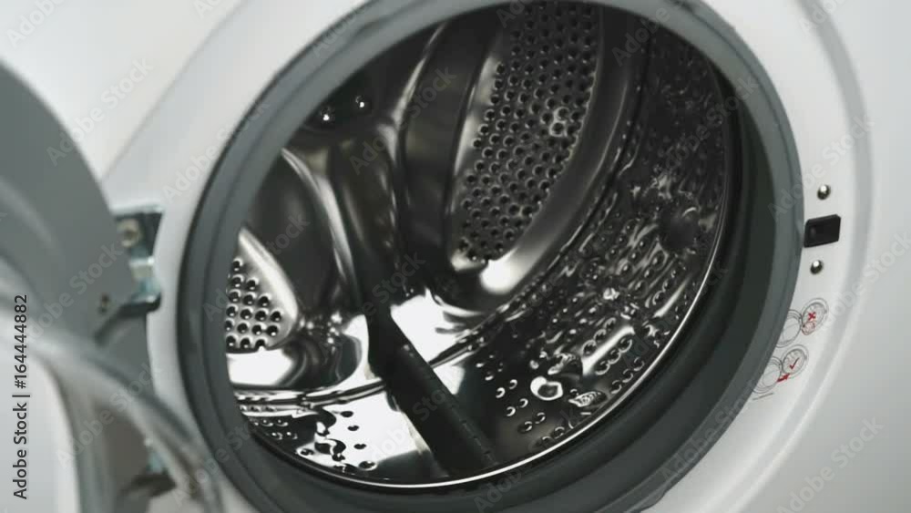 Person's hand puts a towel inside the steel drum of the washing machine. White washing machine with front-loading laundry, door of laundry load with clear glass for monitoring operation. Close-up Person's hand puts a towel inside the steel drum of the washing machine. White washing machine with front-loading laundry, door of laundry load with clear glass for monitoring operation. Close-up