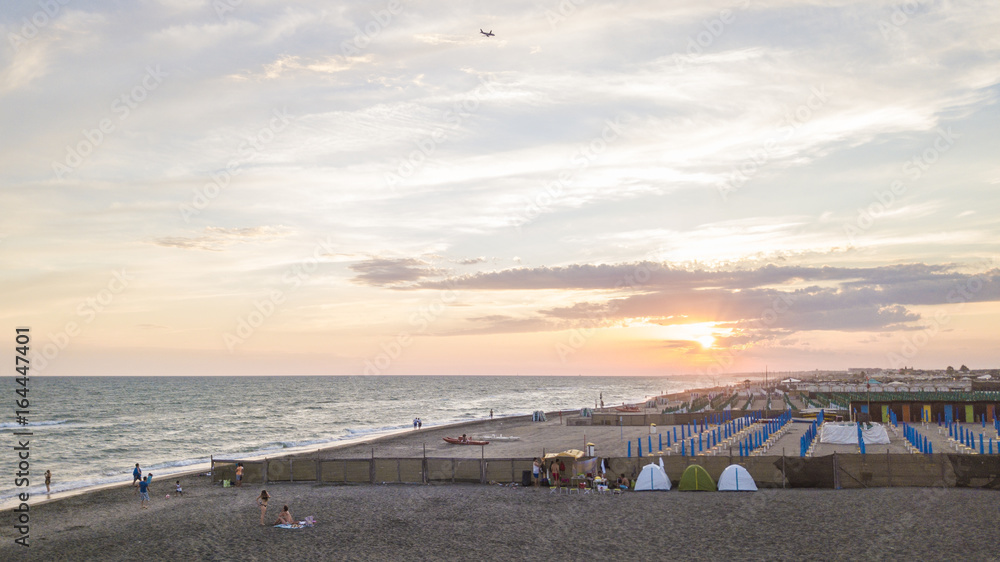 Vista aerea della costa di Ostia al tramonto mentre passa un aereo in direzione Roma. Sulla spiaggia i bagnanti si preparano a lasciare il mare. Gli ombrelloni del lido sono ormai chiusi.