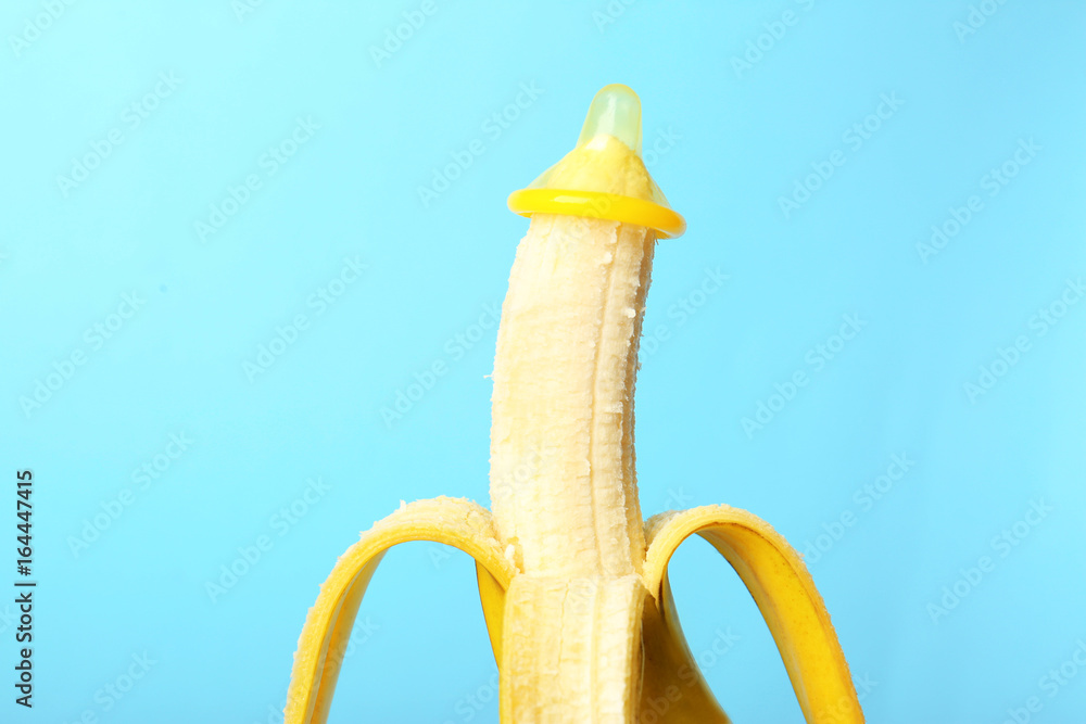 Condom on banana against color background. Safe sex concept - obrazy, fototapety, plakaty 