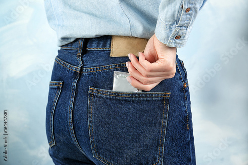 Fototapeta Naklejka Na Ścianę i Meble -  Woman pulling out condom from jeans pocket on light background. Safe sex concept