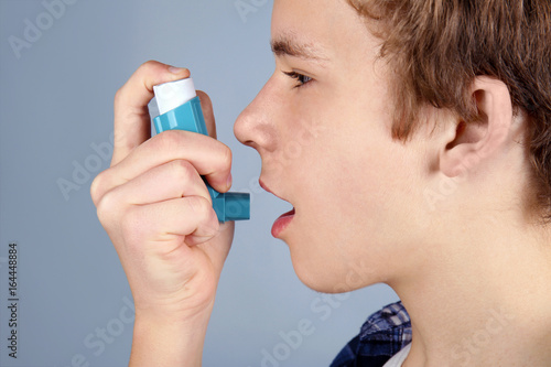Young boy using inhaler for asthma and respiratory diseases on light background