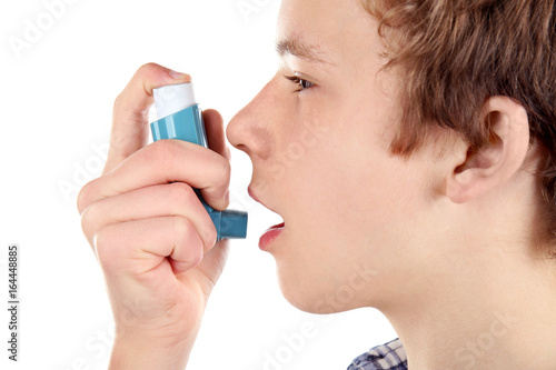 Young boy using inhaler for asthma and respiratory diseases on white background