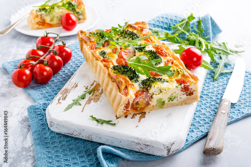 Delicious vegetarian homemade pie, Quiche with cherry tomatoes, broccoli and herbal cheese on old white cutting board. Healthy food concept.