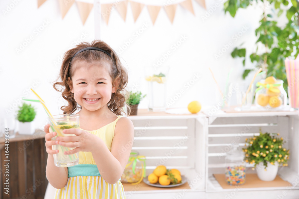 Cute little girl holding glass and blurred stand with lemonade on background Cute little girl holding glass and blurred stand with lemonade on background