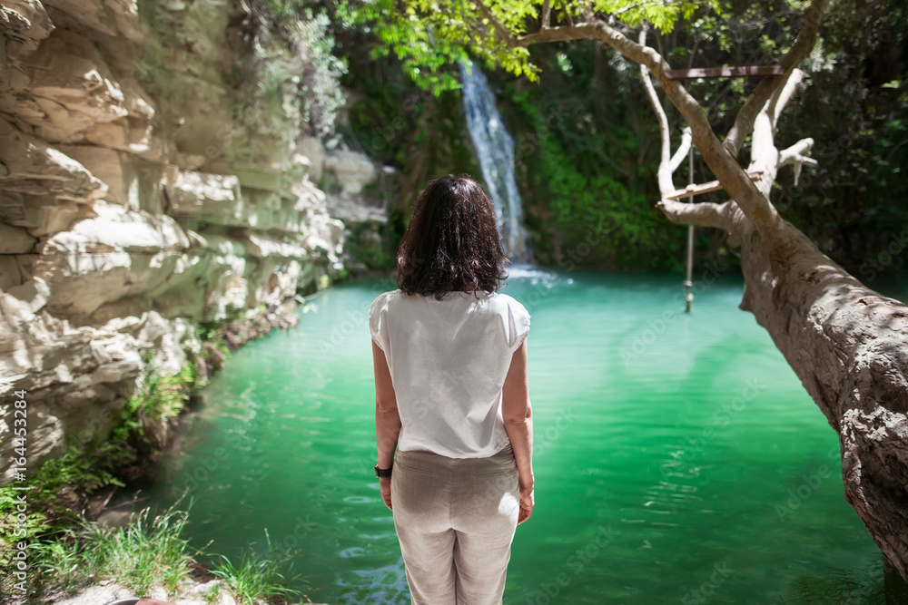 Fototapeta premium Back view of young woman enjoy waterfall on beautiful lake