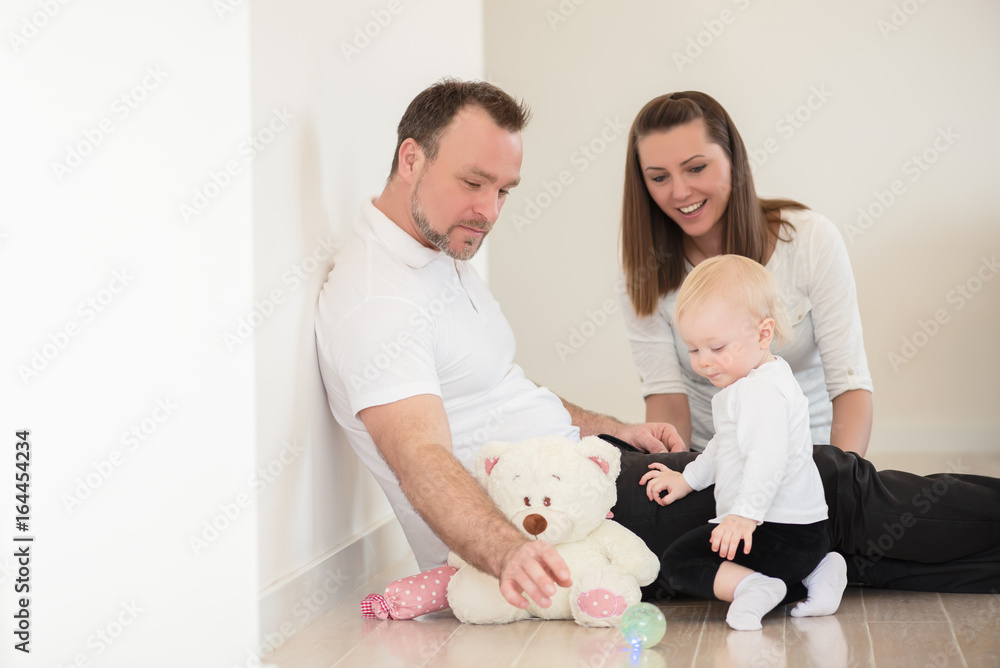 Happy family of three is enjoying at home. Parents and their beautiful baby girl sitting on the ground and playing with ball. Family values. Leisure together. Happy family of three is enjoying at home. Parents and their beautiful baby girl sitting on the ground and playing with ball. Family values. Leisure together.