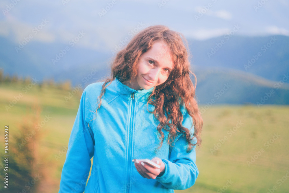 Curly girl texting on smartphone in the mountains during sunset