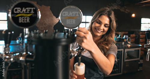 Bild auf Leinwand Female bartender tapping craft beer in bar