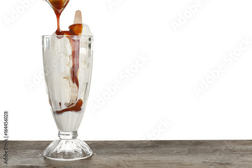 Pouring caramel sauce onto vanilla ice cream in dessert glass against white background