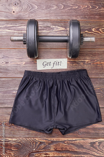 Get in form with body training. Running shorts and dumbbell, wooden background. photo