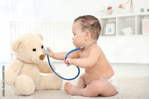 Cute little baby with stethoscope and toy bear playing at home. Health care concept photo